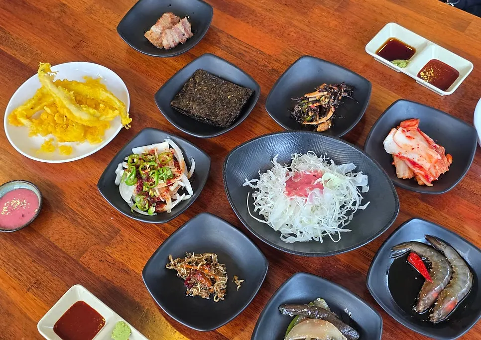 A full spread of side dishes including soy-marinated shrimp and stir-fried anchovies