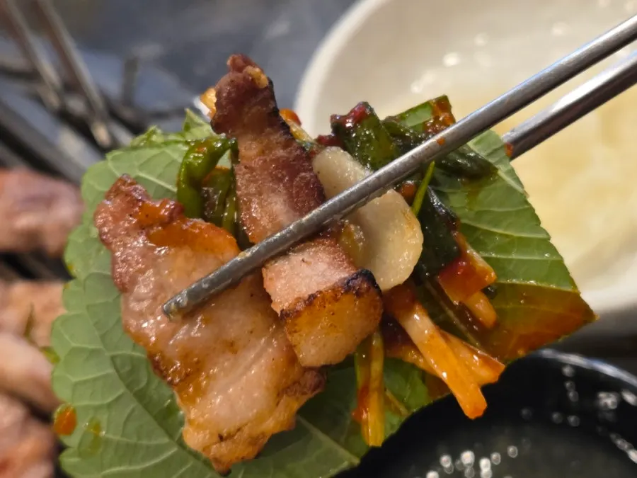 One bite with two pieces of meat topped with garlic and green onion kimchi