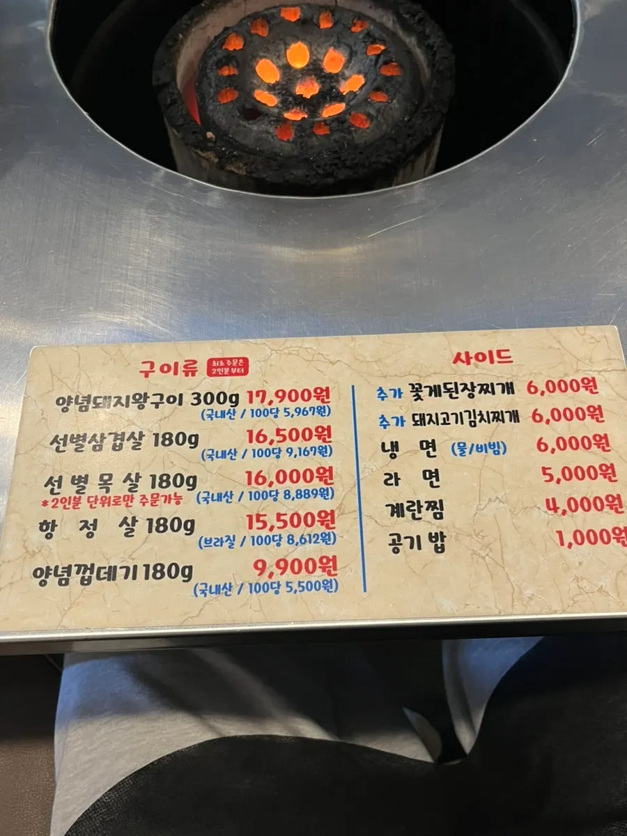A staff member pre-grilling meat over charcoal