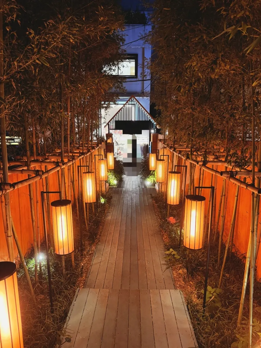 Wooden deck entrance lined with bamboo grove and lantern lighting