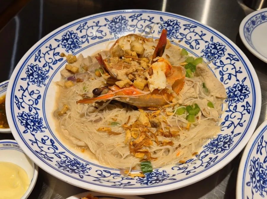 A plate of shrimp broth fried noodles topped with a king prawn