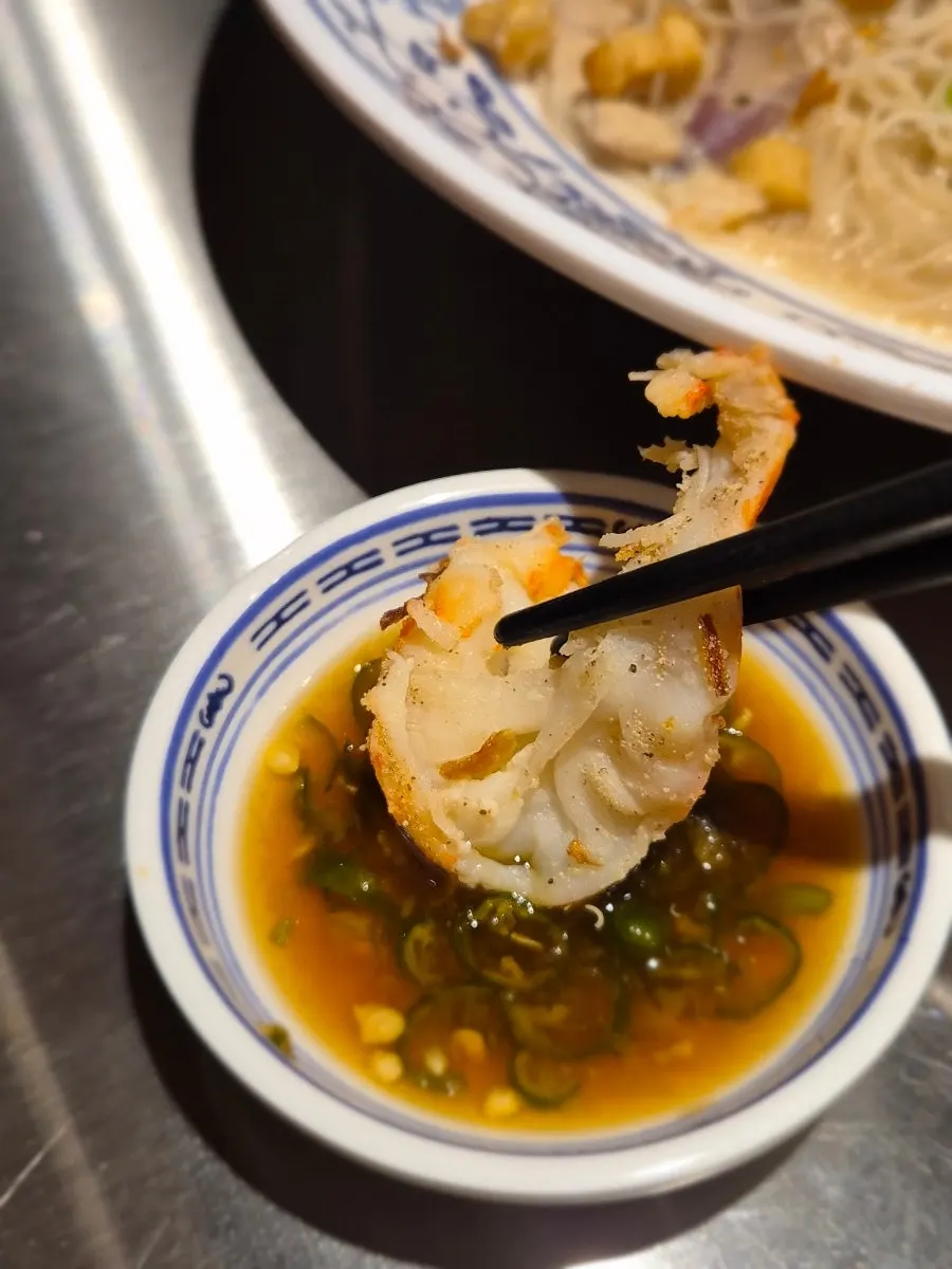 A piece of king prawn dipped in seasoned sauce