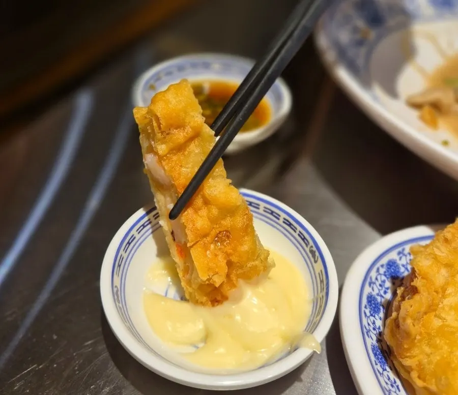 A fried shrimp roll dipped in sauce