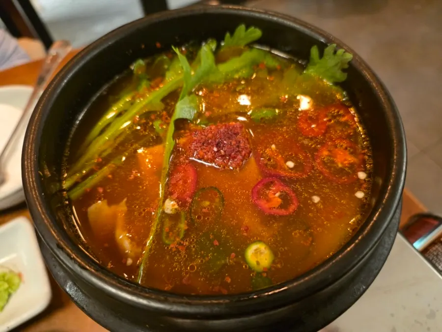 Spicy fish stew in a stone bowl with crown daisy and chili