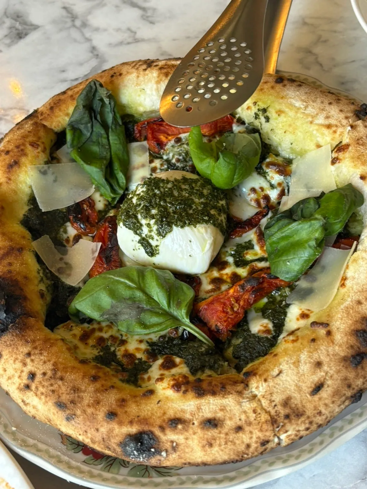 Close-up of the wood-fired basil pizza topped with burrata cheese in the center