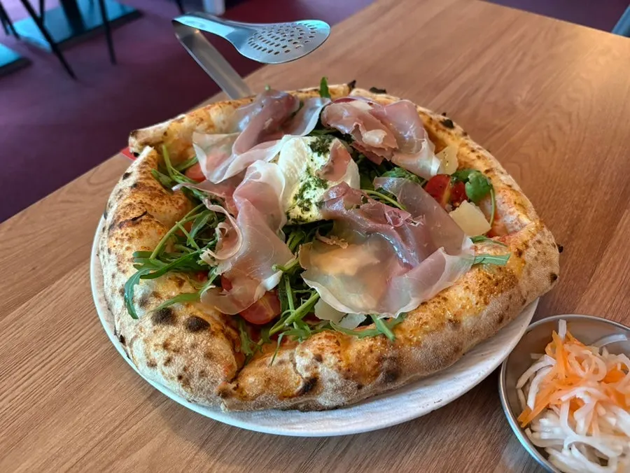 Close-up of the wood-fired pizza topped with arugula and jamón