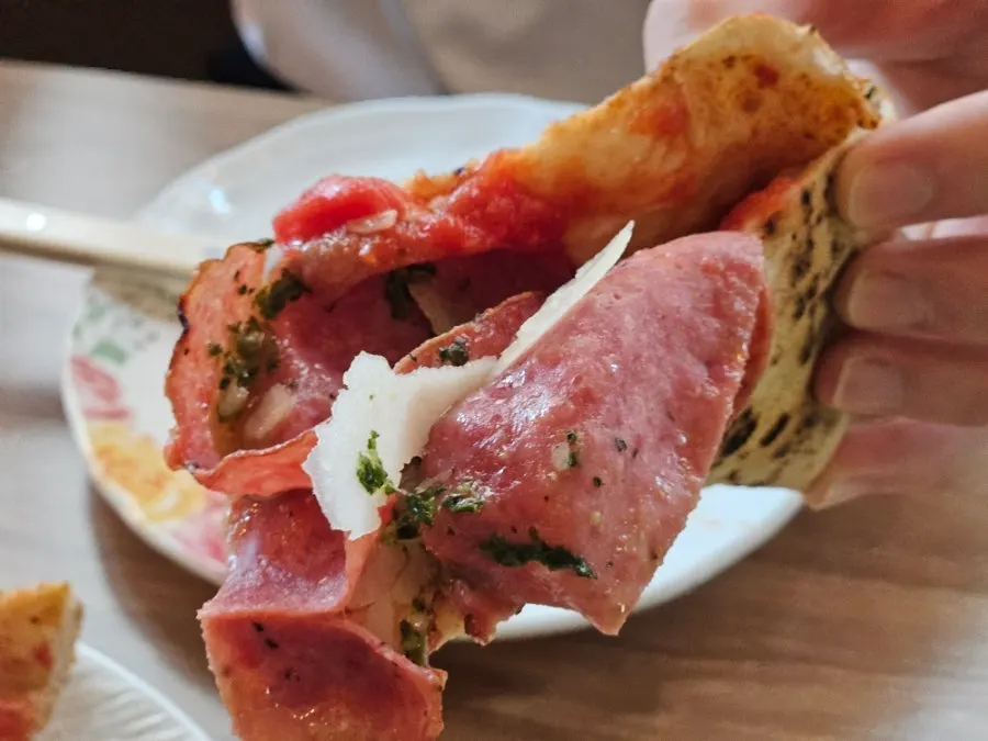 A slice of pizza topped with salami and basil