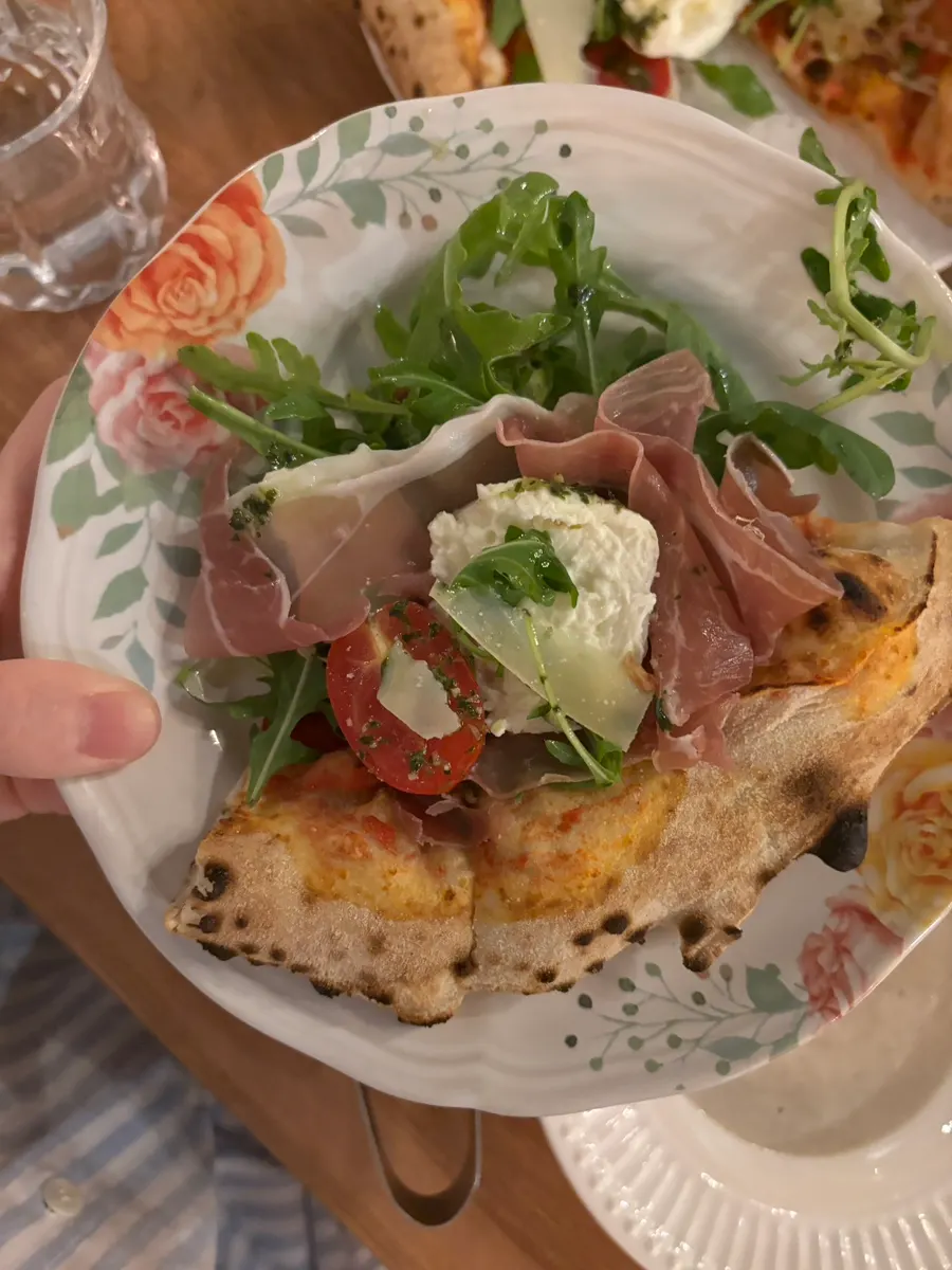 Close-up of pizza topped with arugula, jamón, and burrata cheese