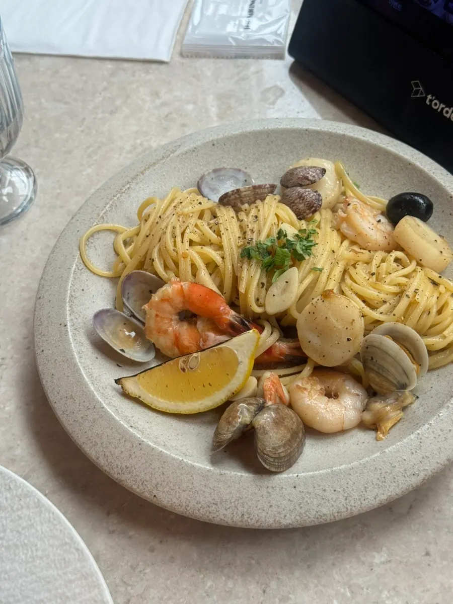 A plate of seafood oil pasta with lemon juice on the side
