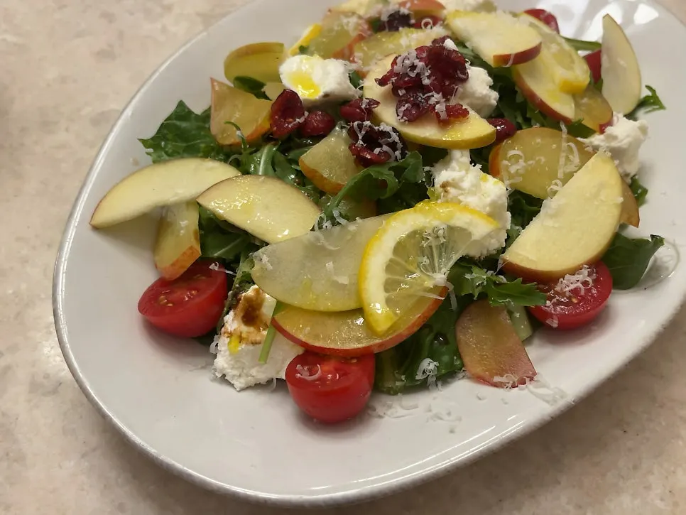 Close-up of ricotta salad topped with arugula and fruit