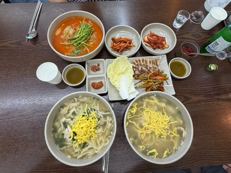 Table spread of two bowls of chicken kalguksu, algoni kalguksu, and bossam