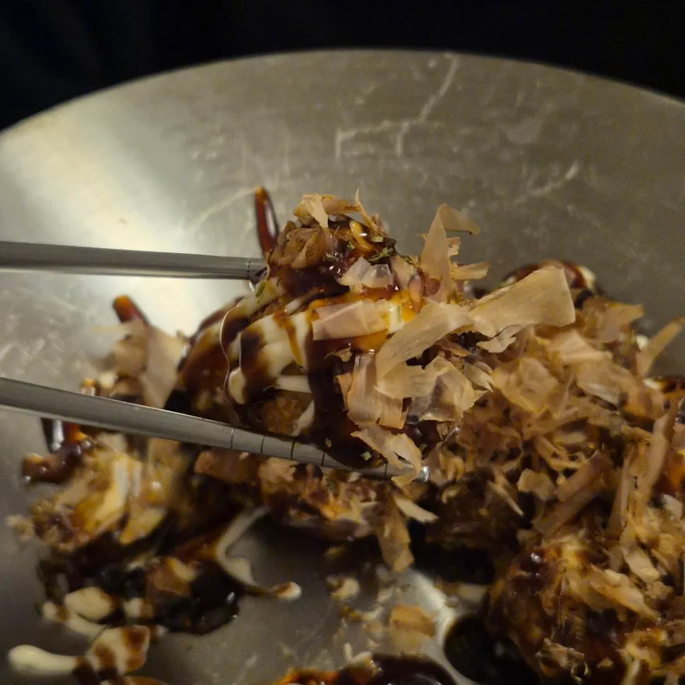 Takoyaki topped with bonito flakes held with chopsticks