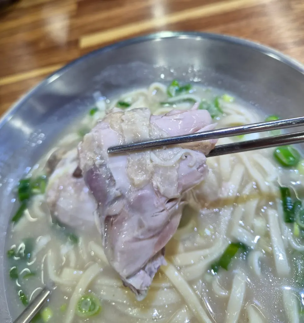 A spoonful of kalguksu broth lifted from the bowl