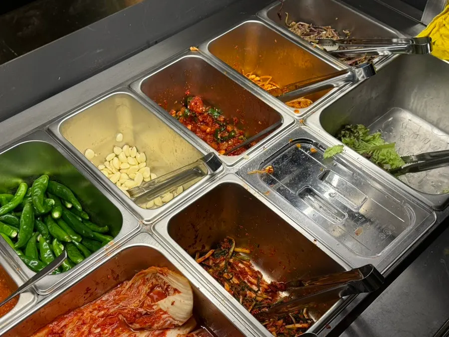 Spread of side dishes including seasoned bean sprouts, bracken fern, and whole kimchi