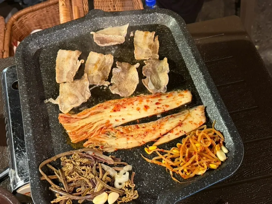 Whole kimchi, bean sprouts, and bracken fern grilling together in meat fat