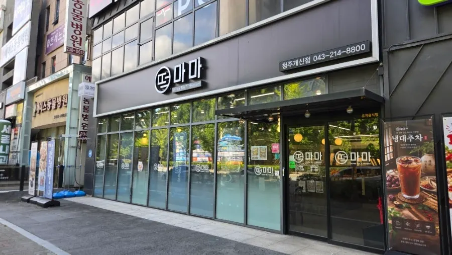 Entrance of Tteokmama Gaesin Branch lit up behind the floor-to-ceiling glass