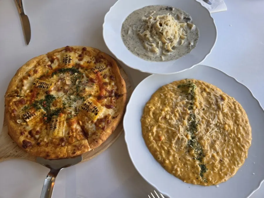 Table spread of corn pizza, pasta, and risotto