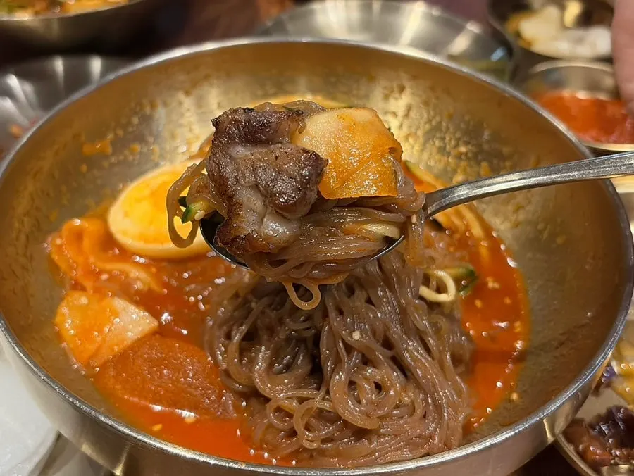 Chewy naengmyeon noodles lifted with chopsticks