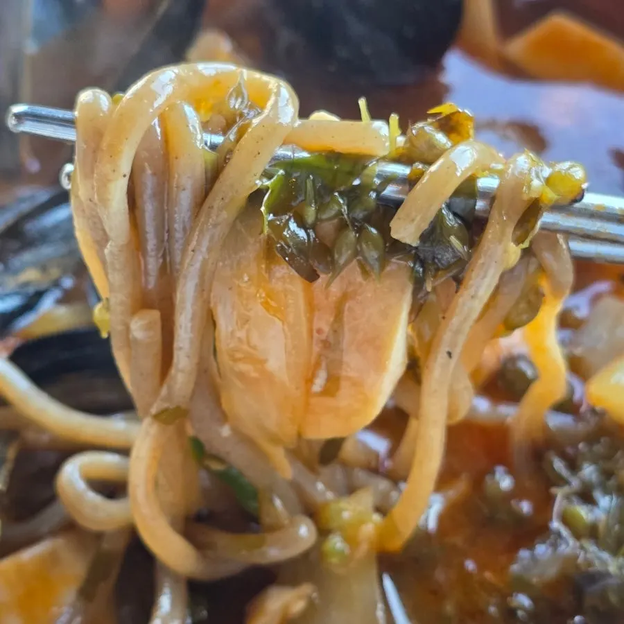 A chopstick lift of noodles and seafood from the ujjam