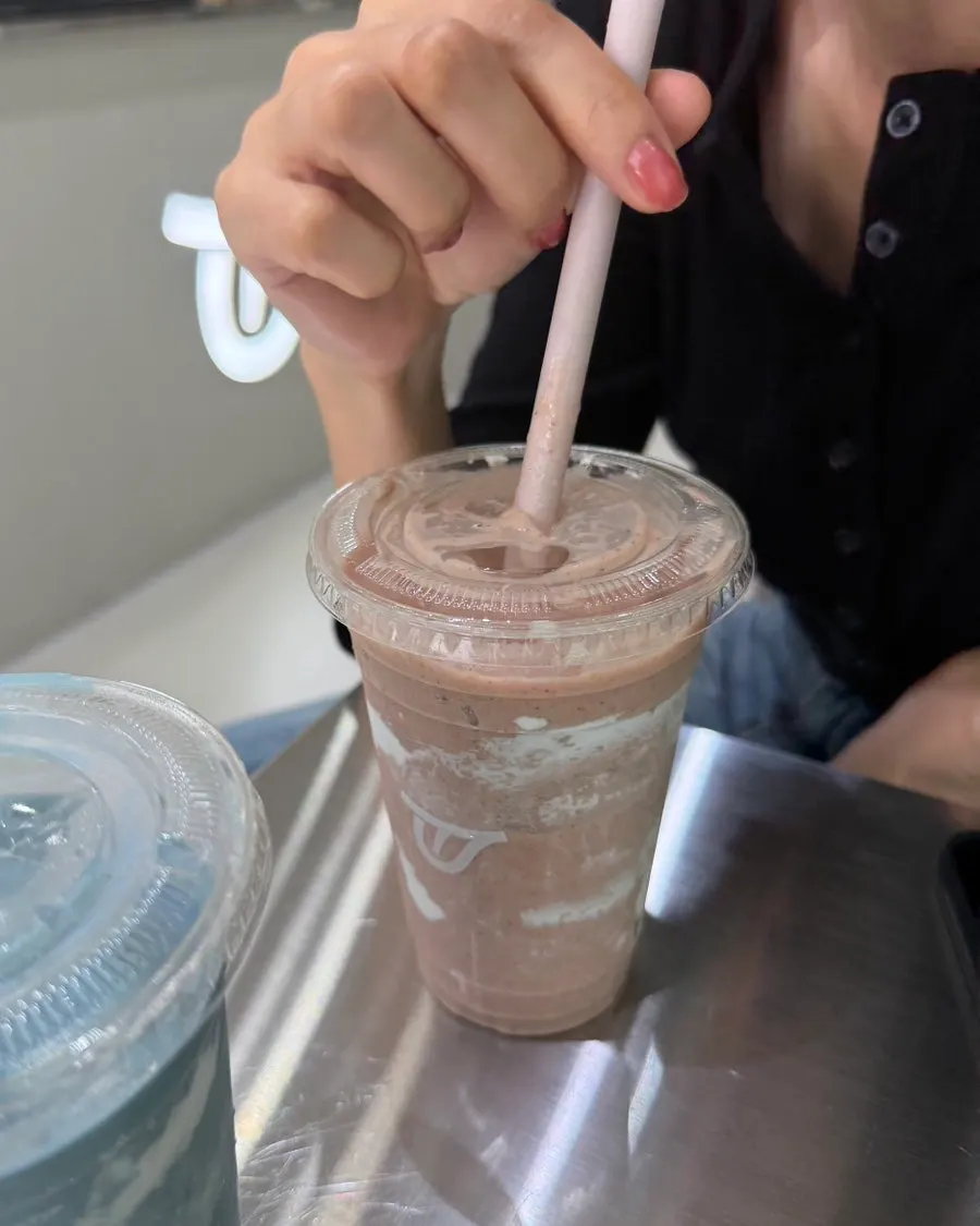 Hand holding a straw over pink Brain Activation smoothie