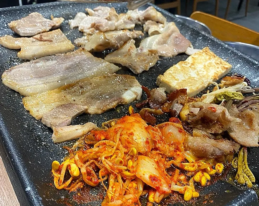 Thin-sliced pork belly grilling with kimchi and bean sprouts