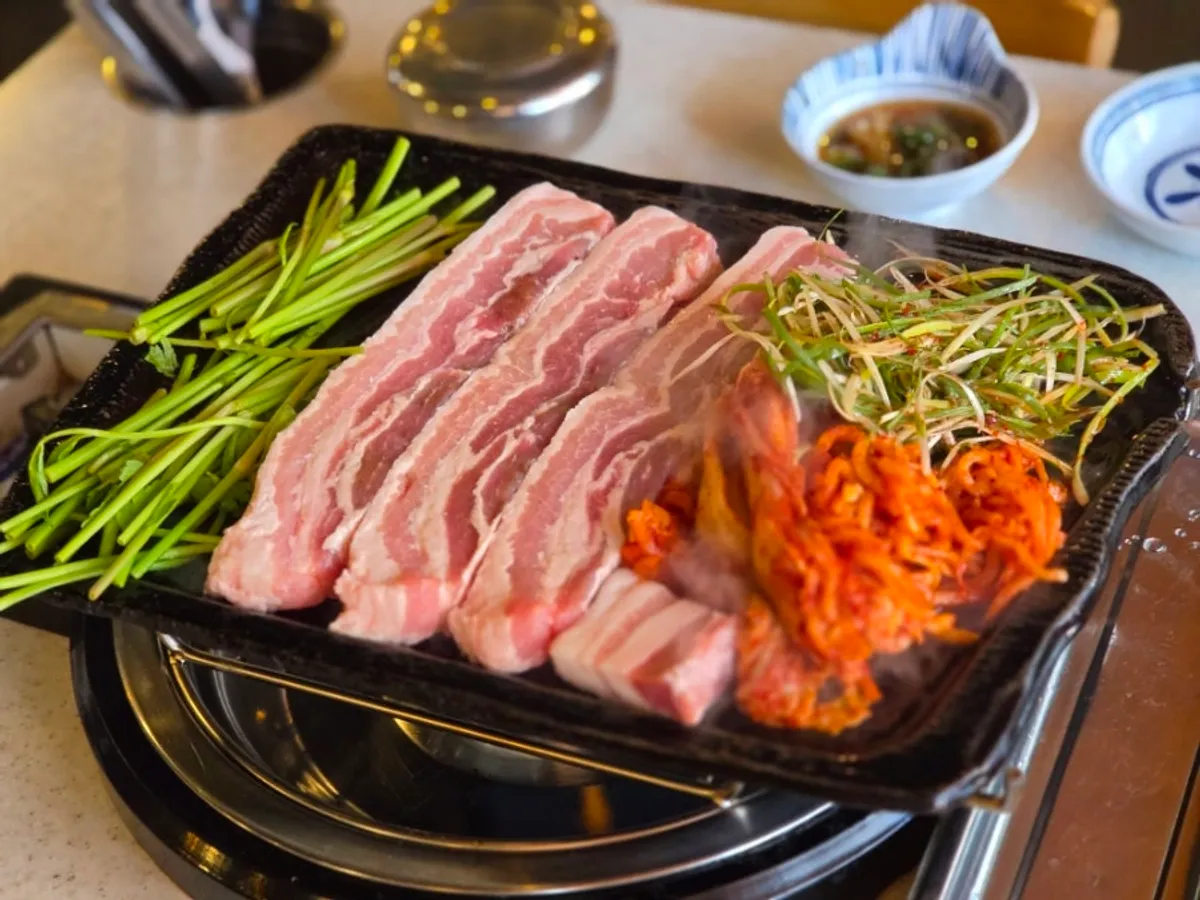 Pork belly, minari, and kimchi laid on the grill