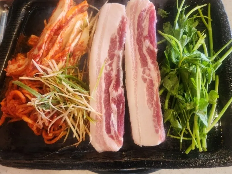 Pork belly, minari, kimchi, and shredded green onion on the grill