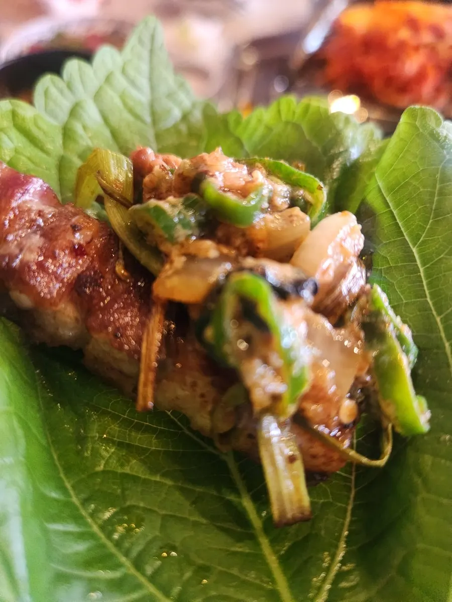 A perilla leaf wrap with pork belly, shredded green onion, and uroeng ssamjang