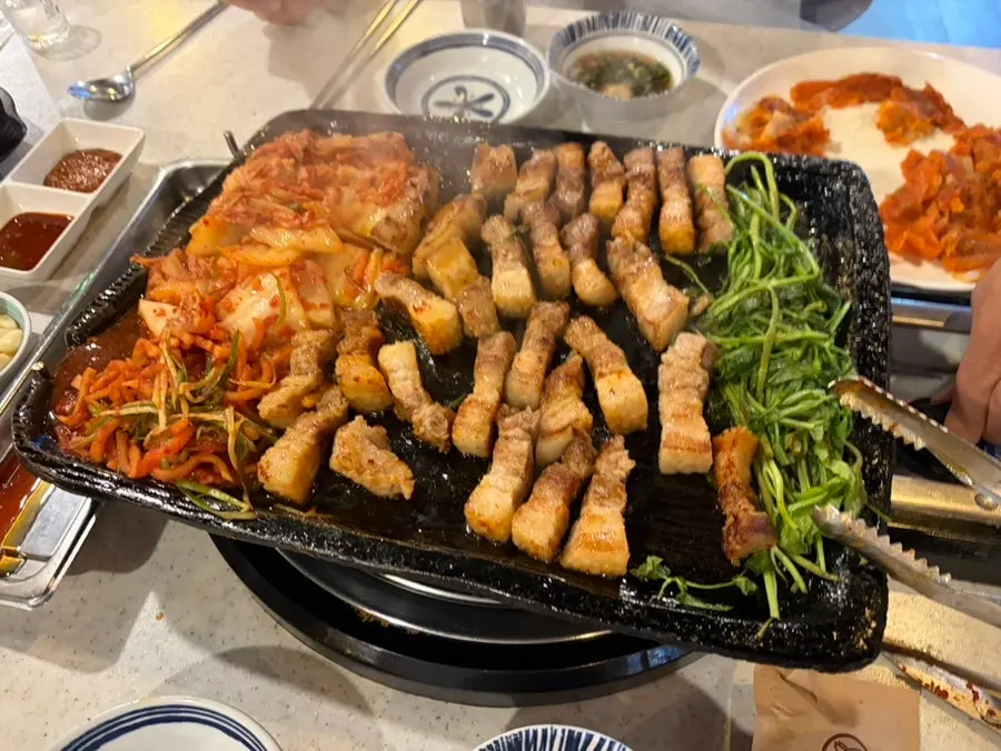 First glass of soju poured next to the grill