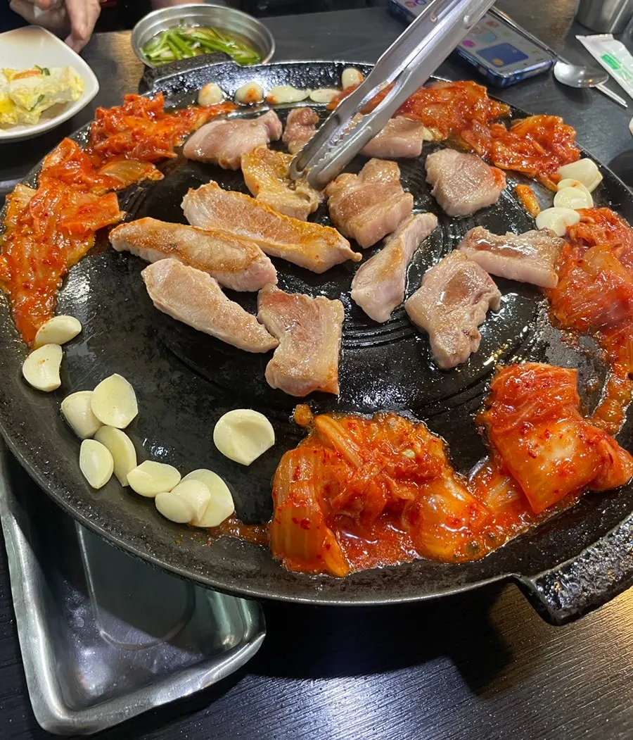 釜蓋の上で焼かれる豚肉とキムチ