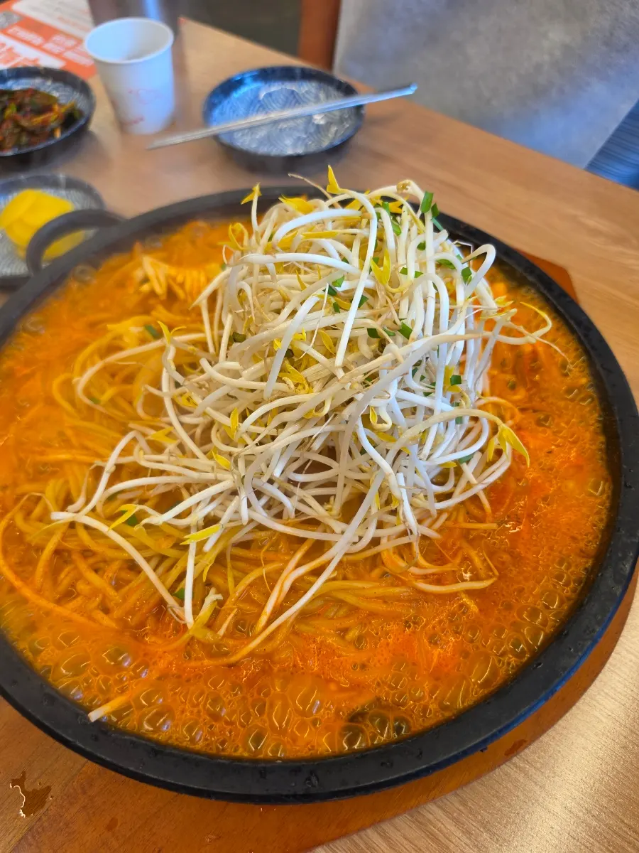 Noodles cooking on top of a layer of bean sprouts in the dol jjamppong
