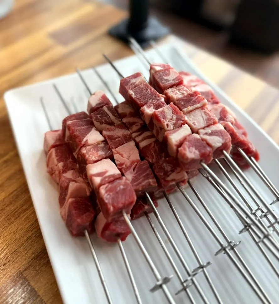 Plate of 8 raw lamb skewers with vivid marbling