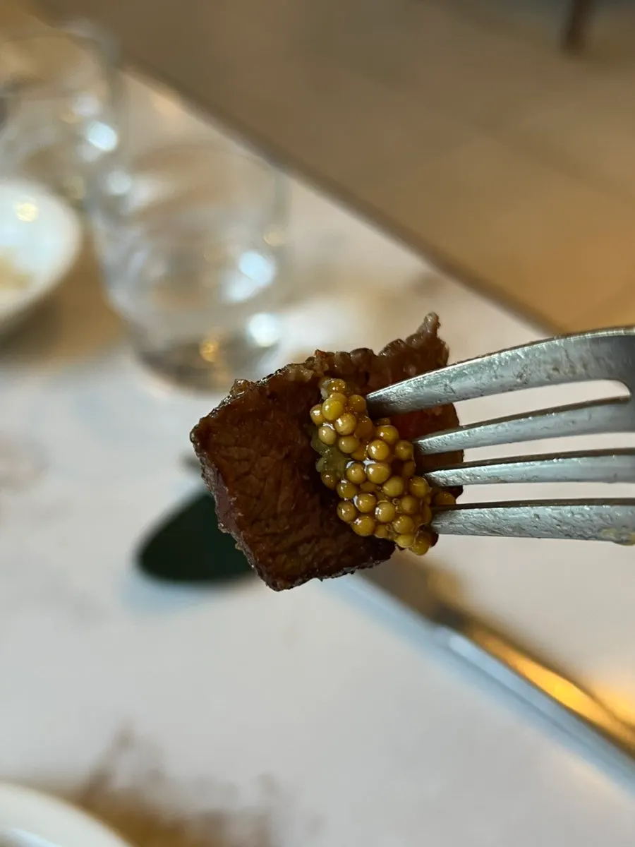 A bite of steak topped with whole grain mustard sauce