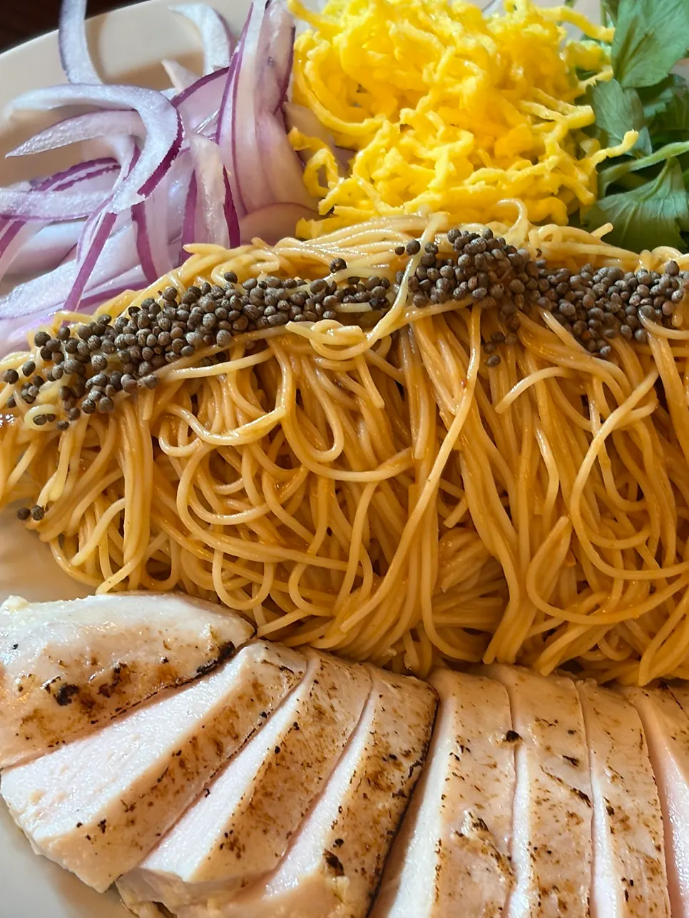 Close-up of chicken breast and green leaves atop the chogye bibimmyeon