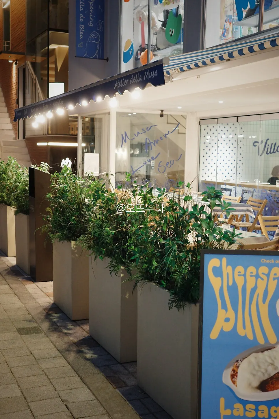 Evening exterior with blue-and-white awning and lit terrace