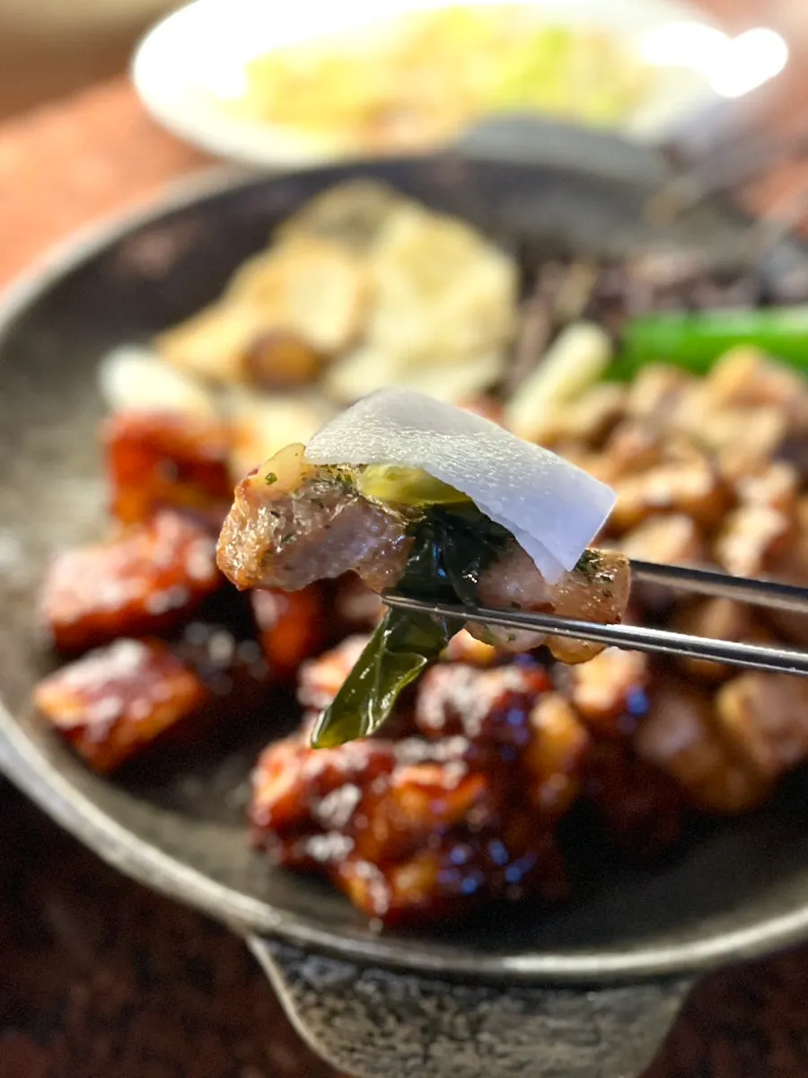A piece of seasoned pork belly held with chopsticks