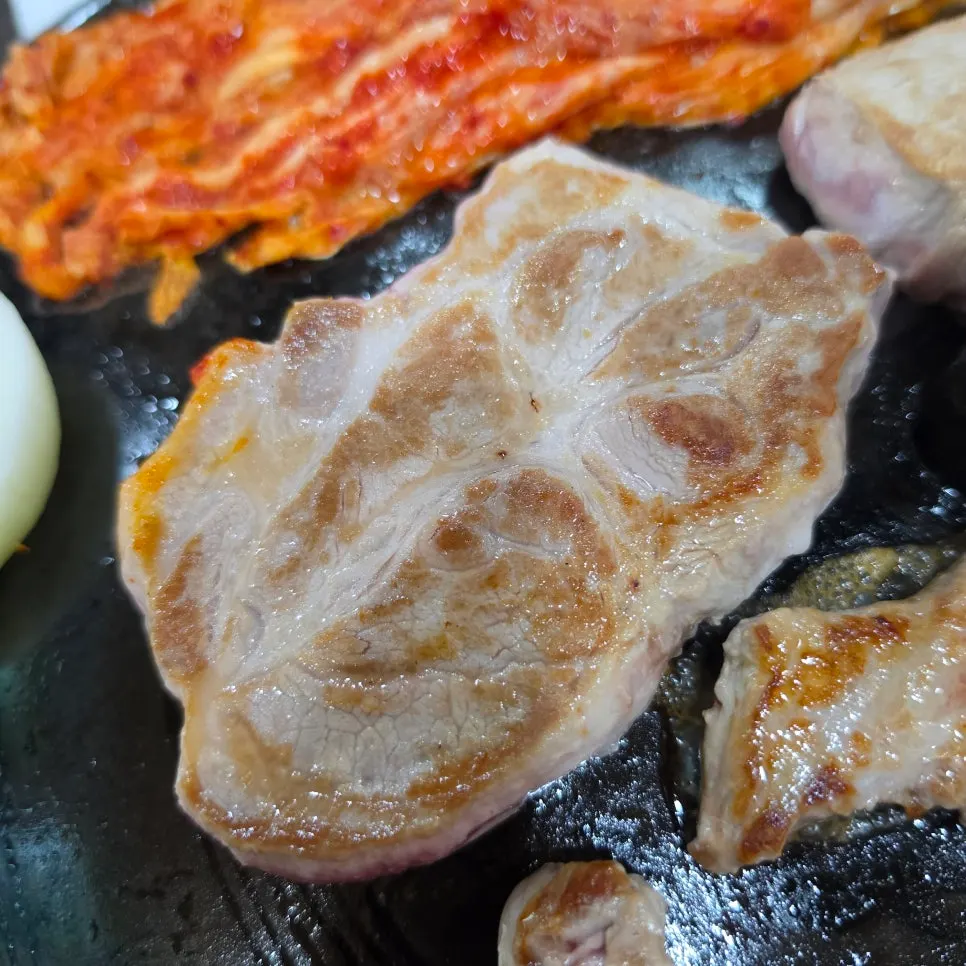 Pork jowl being grilled on the cauldron lid