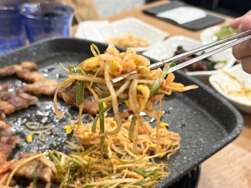 A piece of meat topped with ssamjang, bean sprouts, and scallion salad
