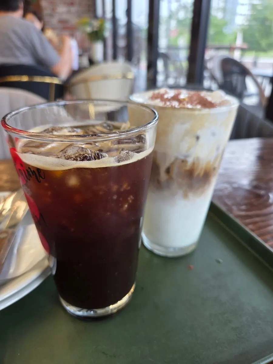 Gold cream latte topped with gold flakes next to an iced Americano
