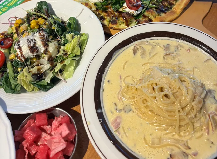 Table with arugula ricotta cheese pizza and two pasta dishes