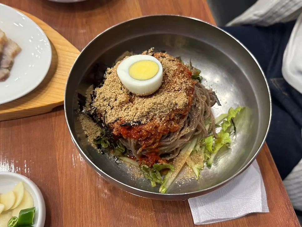 Bowl of bibim makguksu topped with sesame powder and boiled egg