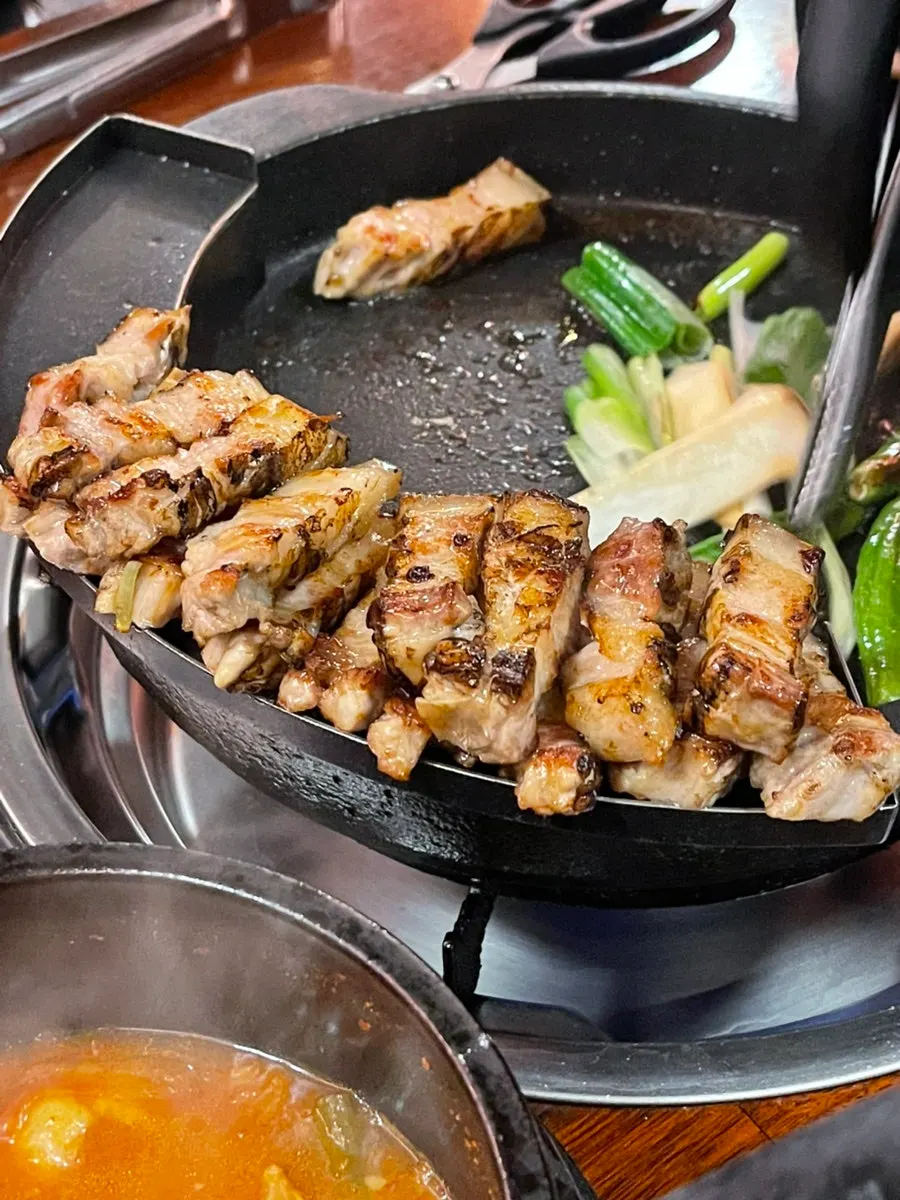 불판 한쪽에 가지런히 놓인 구운 삼겹살과 야채