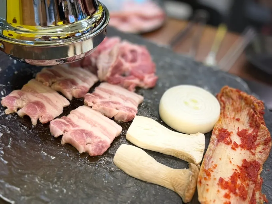 Samgyeopsal, mushrooms, onion, and kimchi on the stone grill