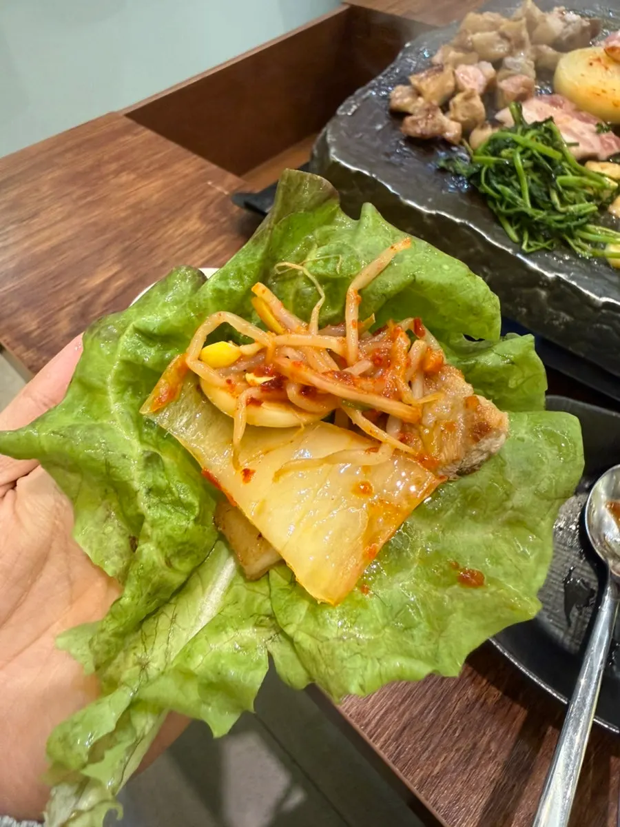 A wrapped bite of samgyeopsal held up