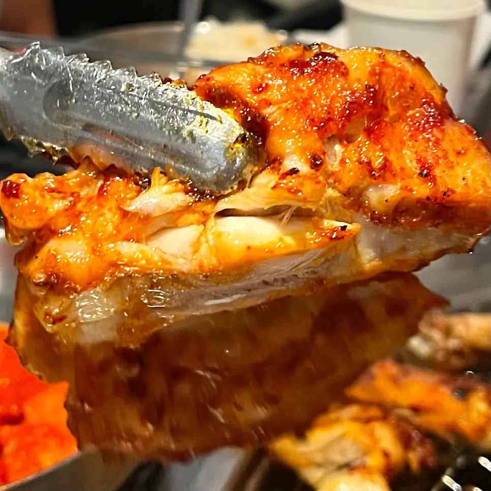 Seasoned chicken galbi cooking at the edge of the grill