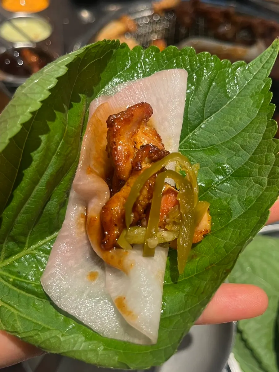 A bite of gochujang dakgalbi wrapped in a leaf