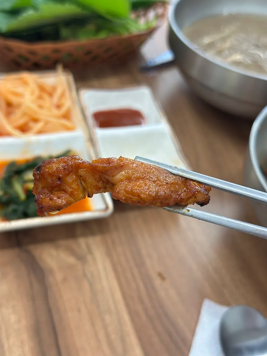 A piece of dakgalbi held with chopsticks