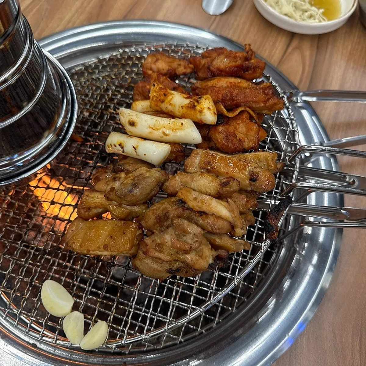 Pre-grilled dakgalbi cooking over charcoal