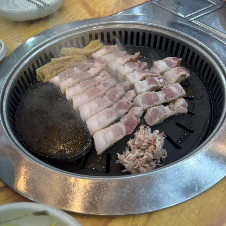직원이 불판에서 두툼한 삼겹살을 굽는 모습