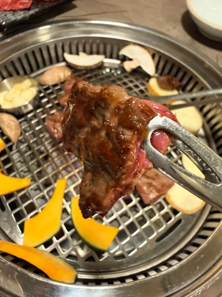 Korean beef grilling over charcoal alongside grilling vegetables